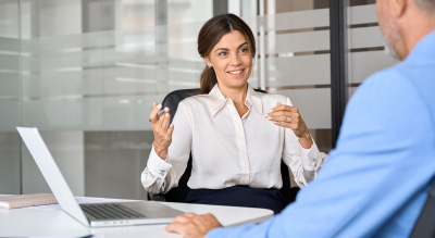 Person at a desk holding a cup while talking, with a laptop in an office