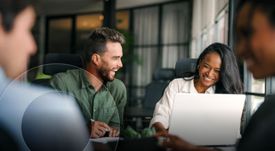 Laughing employees conduct a meeting with a laptop open in front of them