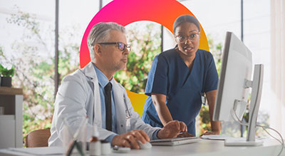 Two healthcare professionals review information together on a desktop computer in a clinical office setting.