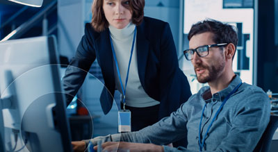 A team of technology professionals collaborates at a computer workstation, reviewing information on multiple monitors in a modern office environment.