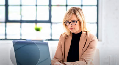 A professional works on a laptop at a desk in a bright office environment.