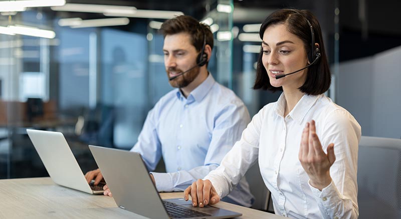 Two colleagues seated at a desk in a modern office collaborate and help a customer