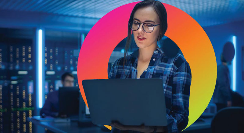 A person using a laptop in a server room environment, representing cybersecurity and IT monitoring.