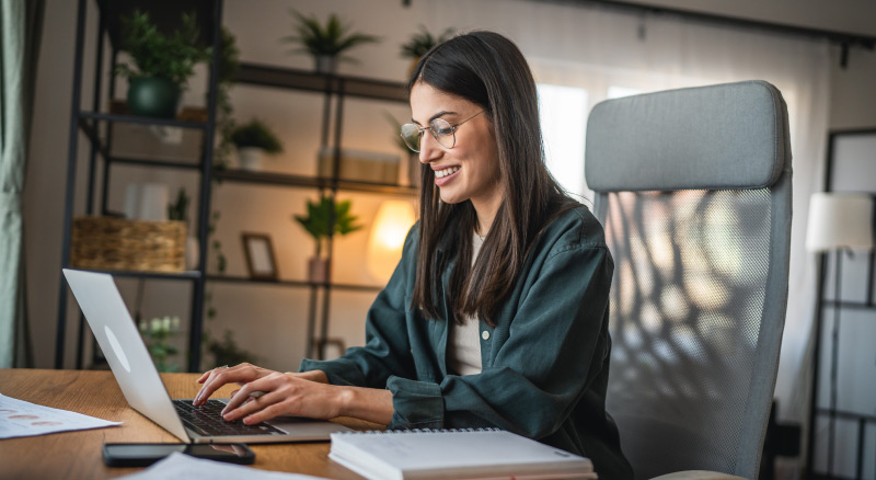 Person working on a laptop at a desk with notebooks in a home office.
