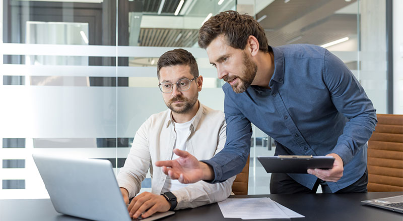 Two businessmen work together analyzing data on a laptop in a bright modern office.