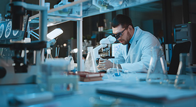 A scientist in a lab coat is intently analyzing a specimen through a microscope amidst various laboratory equipment.