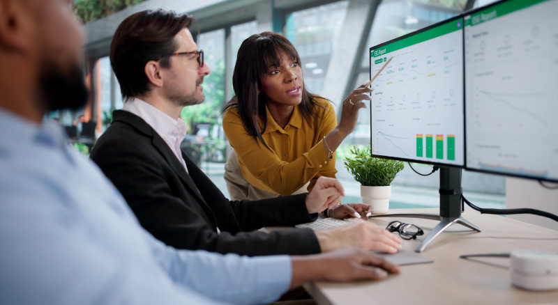 Two people reviewing data on large monitors, with one pointing at charts on the screen.