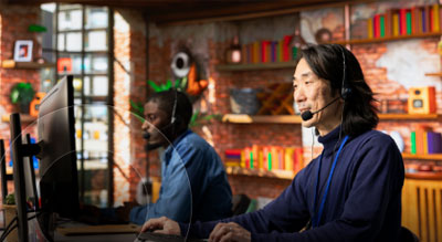 Two people wearing headsets work at desktop computers in a modern office setting