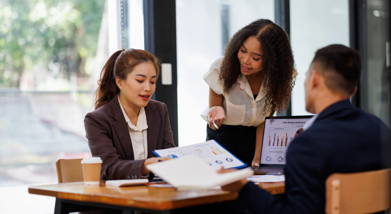 Three people reviewing charts together at a table with a laptop.
