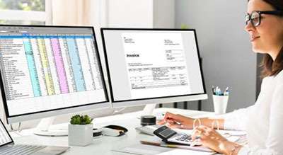 A woman focused on her computer, using a calculator alongside a spreadsheet for her work.
