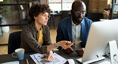 Two people in an office working on papers and a computer