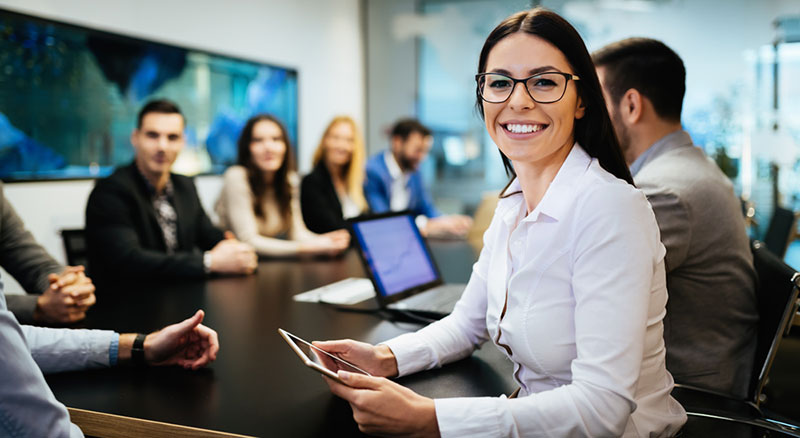 Professional holds a smartphone while seated at a conference table with colleagues in a modern meeting room.