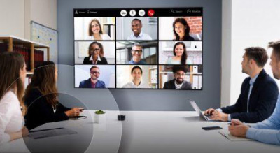 Group seated at a conference table with a large video call displayed on a wall screen