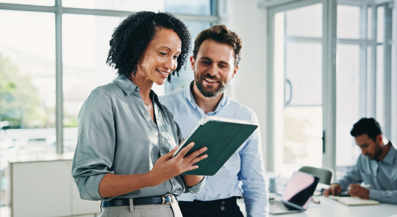 Two coworkers looking at a tablet together in a bright office.
