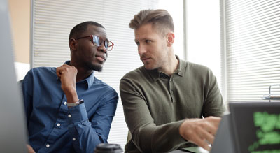 Two coworkers leaning in and discussing data on a laptop in an office setting.