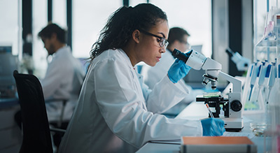 A person in a lab coat and gloves is using a microscope in a laboratory