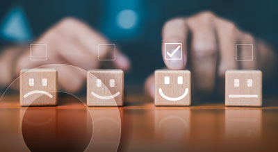 Hand selecting a smiling face block from a row of wooden blocks representing customer satisfaction ratings.